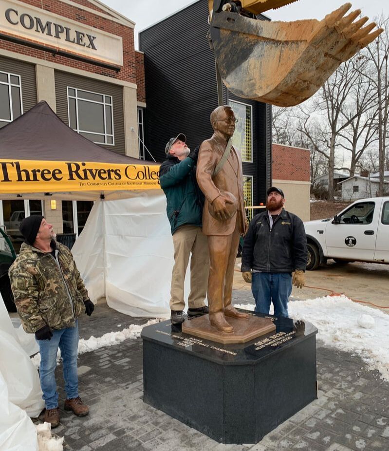 Thank you TRC's Rob, Guy, Adam and Shawn. You made installation in freezing temps a breeze. National Sculptors' Guild Fellow Gary Alsum is in Poplar Bluff, Missouri to install and dedicate the the Gene Bess portrait at Three Rivers College. Special thanks to the school for lending a hand, and creating a beautiful inscribed base for the bronze.  You can find the sculpture on the entry plaza of the Libla Family Sports Center.  The bronze depicts the coach with basketball in hand wearing his familiar suit and tie.  We are very proud to be part of honoring Coach Bess and hope the presence of the sculpture at Three Rivers College brings continued good fortune to the basketball team's success. ​ Coach Bess won a record 1,300 wins in 50 seasons as Three Rivers head coach while teaching two classes a semester, and serving as the Three Rivers Athletic Director throughout his career. At least 42 former players for Bess have gone on to coach all over the country.  He became college basketball’s all-time wins leader in 2001 when he surpassed North Carolina’s Dean Smith and Richard Baldwin of Broome Community College. He was the first college basketball coach to reach 1,000 wins in 2006, the first with 1,100 wins four seasons later, and 1,200 in 2015. His 1,300th win came in what ended up being his final home game on a court named in his honor. Coach Bess finished with a career record of 1,300-416, won national championships in 1979 and 1992, coached in four national title games, appeared in 17 national tournaments, won 23 region championships, and is a member of four halls of fame.