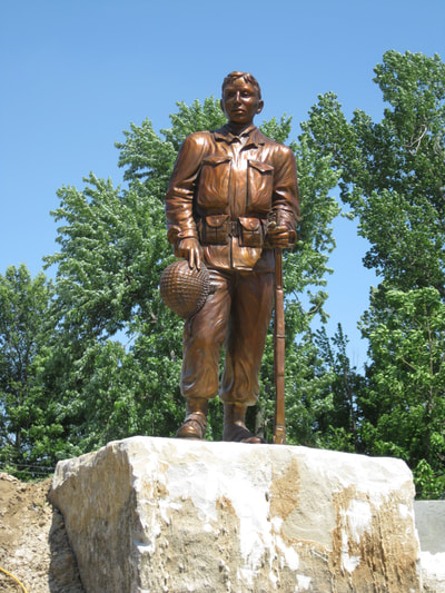 "Honor" by Gary Alsum, National Sculptors'  Guild
One of the first sights you will see when you turn onto Main Street from Highway 49 is the Veterans Memorial Park of Rector. A life-size bronze sculpture of a World War II soldier stands at-rest atop a native Arkansas boulder in the center. Created by Artist/Sculptor Gary Alum, the soldier is a stunning tribute to every man and woman who has served or is serving in any branch of the United States Armed Service.
Presiding over the park flies the flag of the United States of America; stretching outward in an arc flies the Arkansas flag, the Rector flag and the flags of each branch of the U.S. Armed Forces, Army, Navy, Marines, Air Force and Coast Guard. You will also see the POW/MIA flag included in the array.
Wide walkways and beautifully maintained landscaping present a welcoming invitation to stroll through the grounds and visit the memorial granite pavers that line the walkways honoring local men and women who have served. The visitor center and park headquarters, formerly the old jail/water office sets at the north end of the park. A founders’ wall stands on either side of the statue to recognize those individuals and organizations who made substantial contributions to the development of the Veterans Memorial Park.
Dedicated in 2011 the park is the product of a collaborative effort of the Veterans Memorial Park Association and the City of Rector Downtown Central, Inc. The land for the park was given to the City of Rector Downtown Central by Mrs. Pauline Crockett, Sherland and Barbara Hamilton, George Jernigan and Robert Jernigan.
Ongoing support for the park is provided by the Veterans Memorial Park Association in partnership with the City of Rector Downtown Central, a Main Street Arkansas program of the Department of Arkansas Heritage.