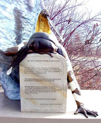 The tombstone of the sculpture reads:   He Who Fights With A Feather ​ ​This memorial pays tribute to the Native Americans who have fought and sacrificed in the many conflicts that our government has chosen to participate.  The kneeling man reaches to Mother Earth in search of strength and comfort.  Behind him stands a symbol of hope, touching his shoulder with an eagle feather, she conveys hope and understanding for a time when conflict may be solved more peacefully.  With honor and respect for all beings.  Sculptor, Denny Haskew NSG Public Art Placement 41 #NationalSculptorsGuild #PublicArt #NSG #DennyHaskew #Figurative #Bronze #VeteransMemorial #IndeginousPeople #BaronaBandofMissionIndians #California #SculptureIsATeamSport #ArtistDriven #ClientMinded
